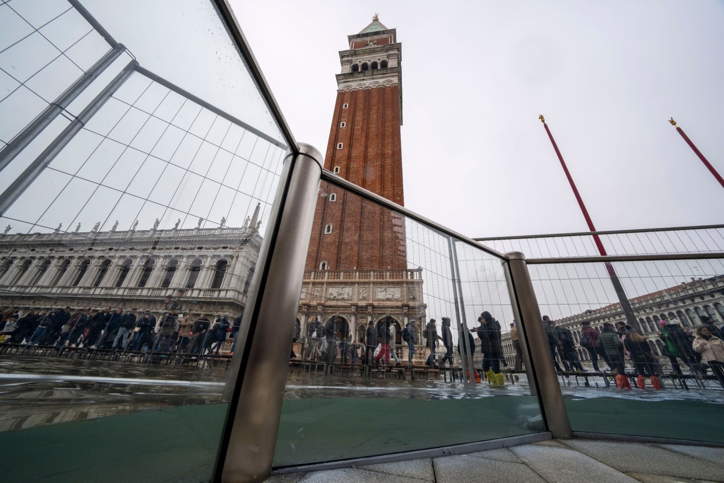 Touristen gehen auf Laufstegen über den überschwemmten Markusplatz.