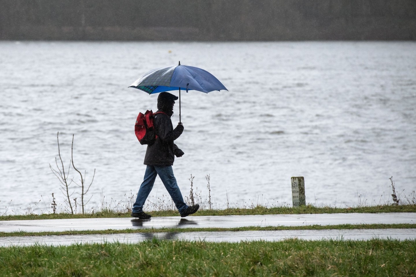 Spaziergänger mit Regenschirm am Ufer des Kemnader Sees in Bochum.