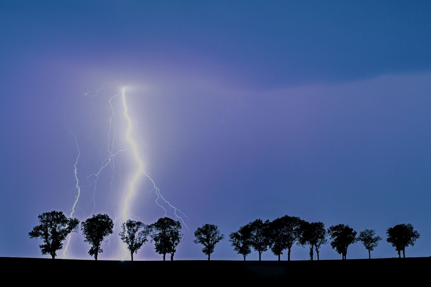 Ein Blitz eines Gewitters erhellt den Nachthimmel über der Landschaft im Osten des Landes Brandenburg.