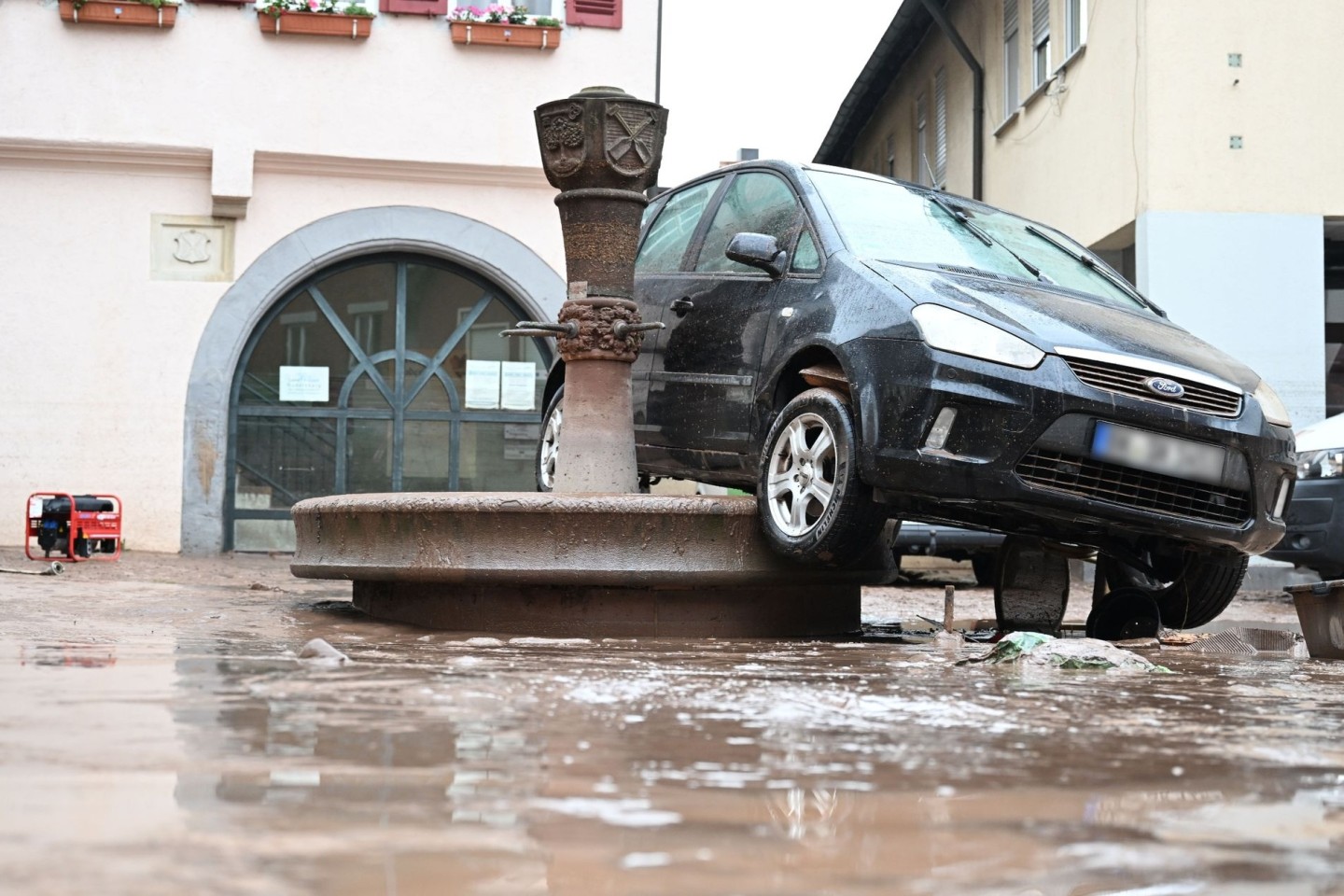 Auf einem Brunnen in Rudersberg hängt ein durch das Hochwasser weggespültes Auto.