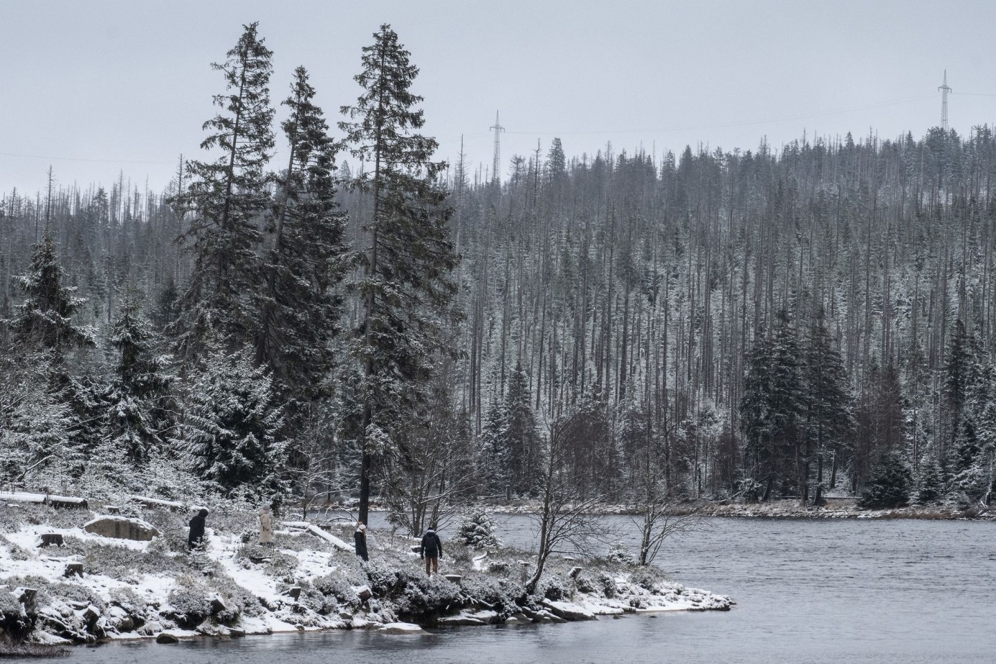 Wanderer gehen am leicht verschneiten Oderteich im Harz spazieren.